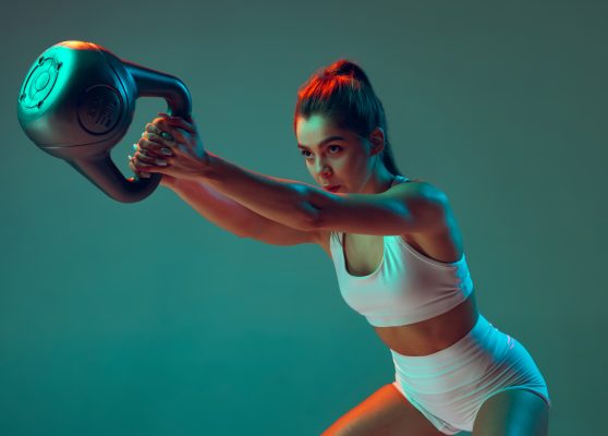 Portrait of young sportive girl doing squats with weight isolated over green background in neon